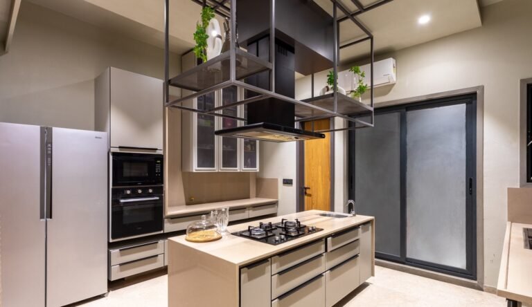 Modern kitchen with stainless steel appliances, hanging shelves, and beige cabinets.