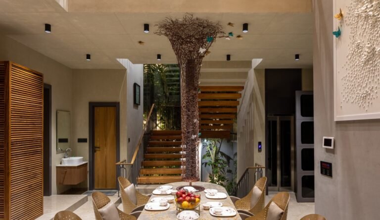 Modern dining room with artistic tree centerpiece, staircase, and decorative wall art.