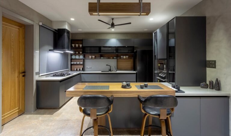 Modern kitchen with wooden bar stools, black appliances, and a ceiling fan.