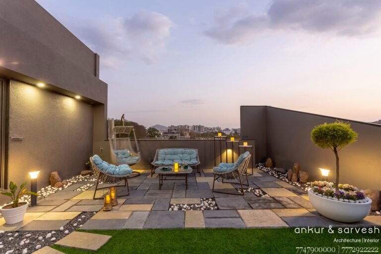 Rooftop patio at dusk with comfortable seating, decorative lighting, and cityscape background.