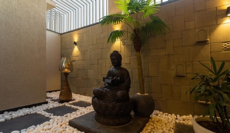 A serene indoor zen garden with a Buddha statue, potted plants, and smooth stones.