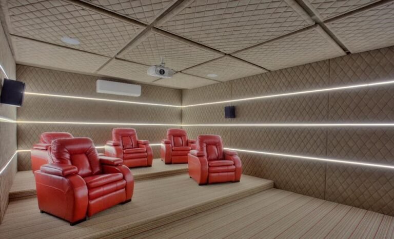 Modern home theater with tiered seating and red leather chairs, ambient lighting, and quilted walls.