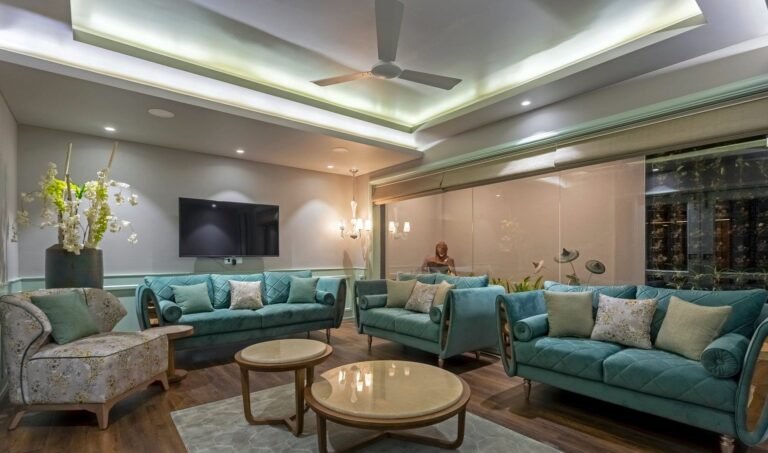 Modern living room with teal sofas, ambient lighting, and a person reading in the background.