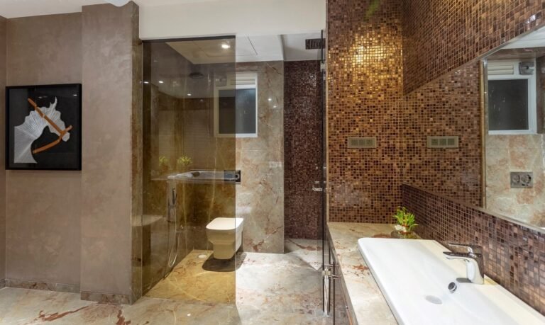 Modern bathroom with beige and mosaic tiles, glass shower, toilet, and bathtub with artwork on wall.