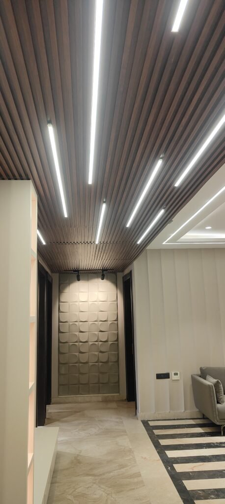 Contemporary hallway interior with wooden slatted ceiling, recessed strip lighting, geometric 3D wall panel, and marble flooring in a luxury living space.