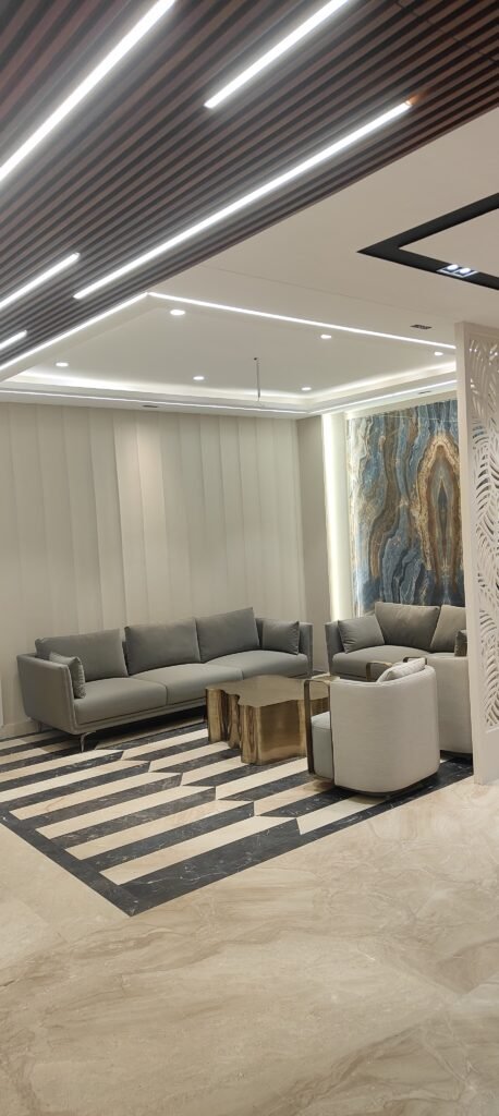 Modern luxury living room interior with grey sofas, abstract onyx wall art, striped marble flooring, wooden slat ceiling, and ambient recessed lighting.