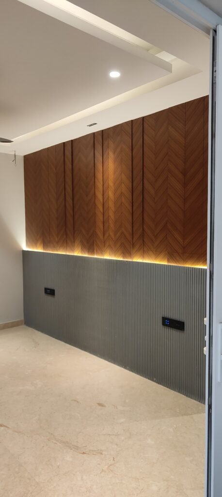 Modern interior featuring a herringbone wood accent wall with recessed lighting above a textured gray panel, complemented by marble flooring.