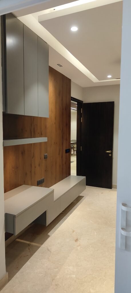 Modern entryway featuring gray cabinetry and a wood-paneled wall, illuminated by recessed lighting, with a sleek dark door at the end.