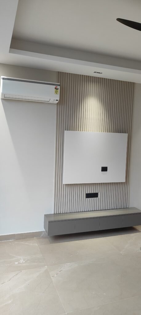 A modern living space featuring an air conditioner, a sleek white wall-mounted panel, and a low gray storage unit against a textured backdrop.