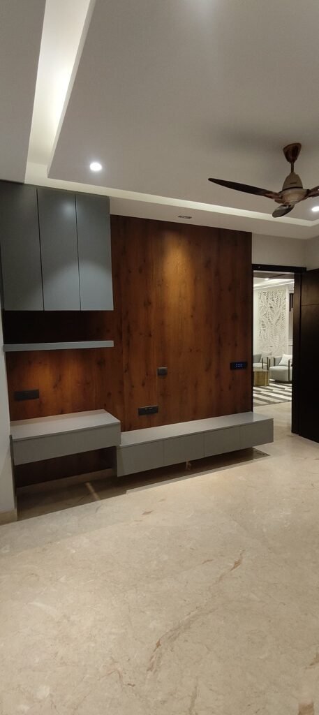 Modern living room with gray cabinetry against a wood-paneled wall, marble floor, and a ceiling fan above. Soft lighting enhances the space.