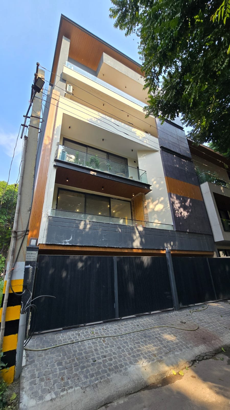 Modern multi-storey residential building with wooden and black panel accents, designed by expert interior designers in South City Gurgaon, with glass balconies and lush greenery.